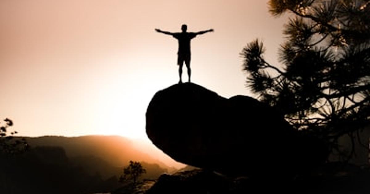 朝日に向かって両腕を広げる人物のシルエット。エッセンシャル思考の象徴のように、不要なものを手放し本質に向き合う姿