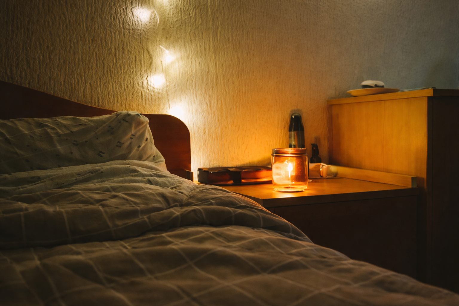 夜の寝室で、ベッド脇の灯りが静かに灯っている様子